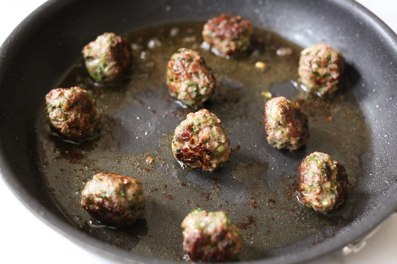 Lamb kofta being browned in oil in a skillet.