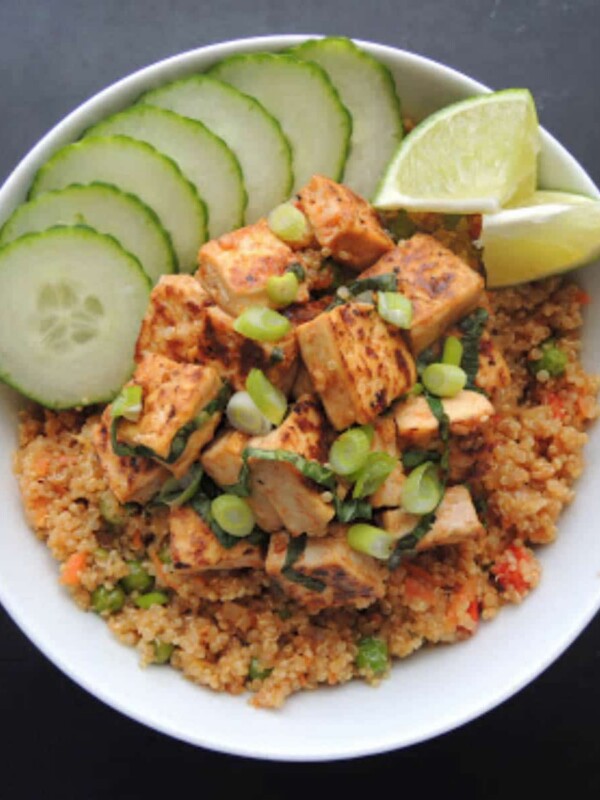 Bowl with basil tofu on a bed of stir fried quinoa garnished with sliced cucumber and lime wedges.