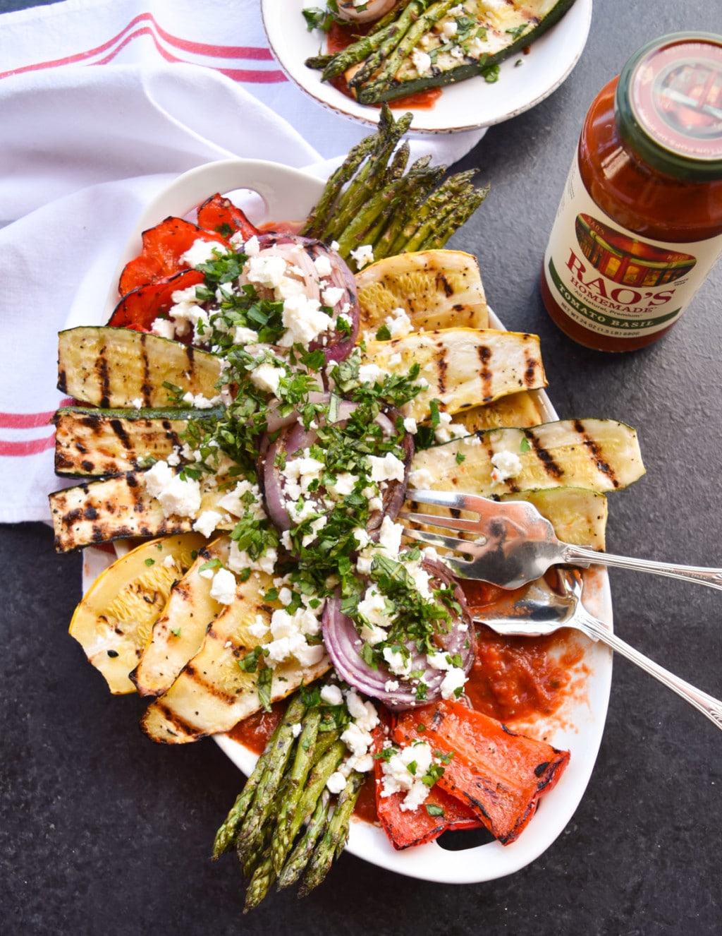 Platter of grilled vegetables with one portion removed and part of a plated serving in the top of the frame.